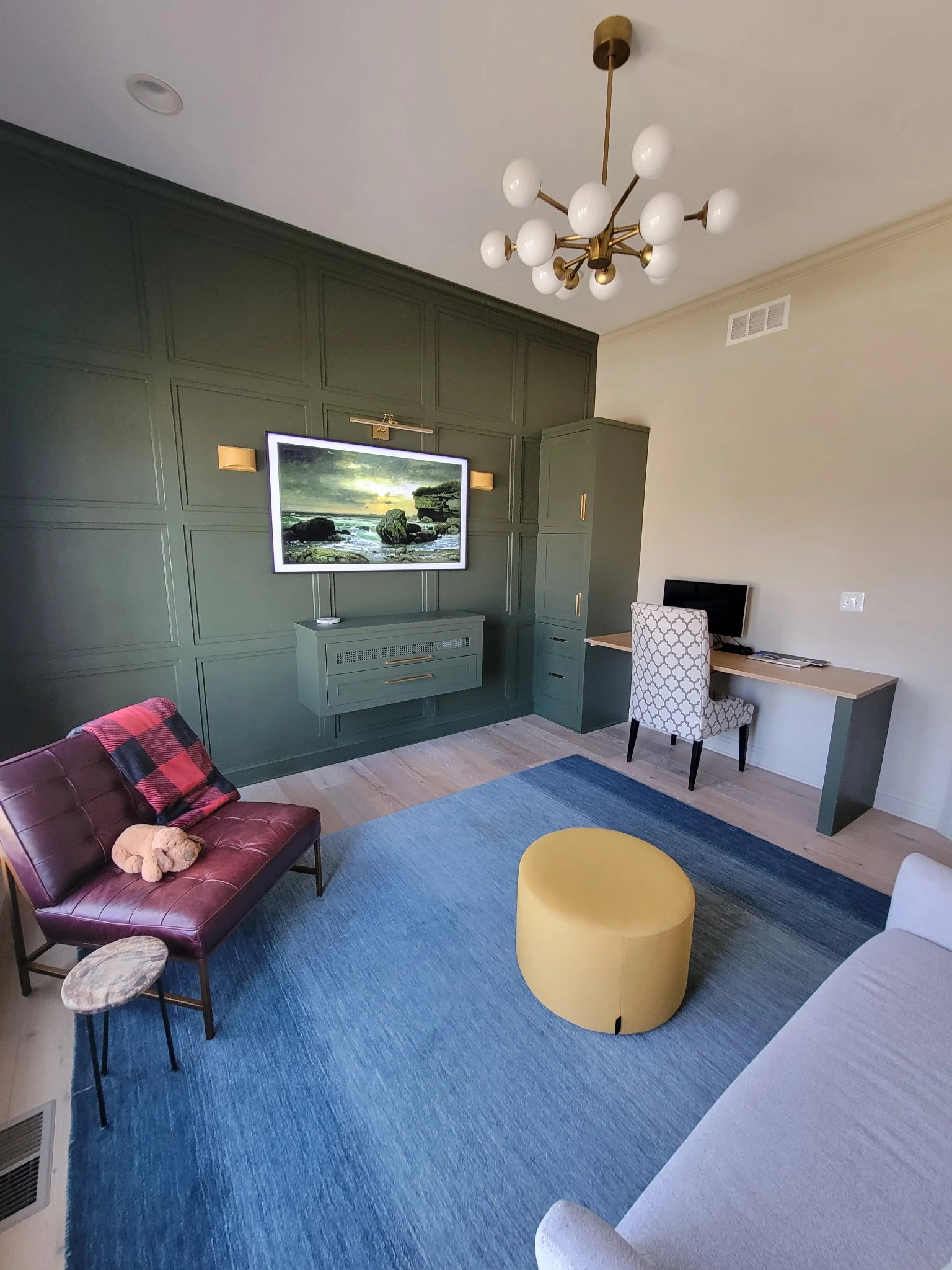 Finished den with custom desk, tall storage cabinet, paneled accent wall, seating area, and wood flooring.