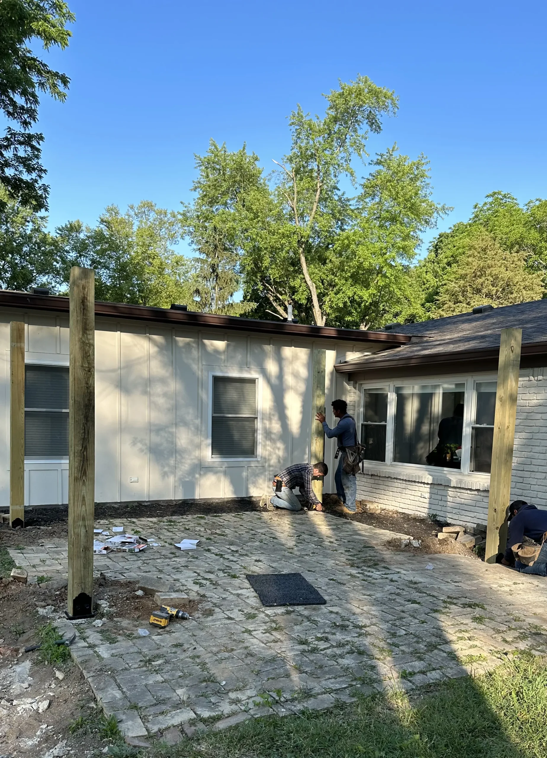 Construction crews installing posts for a custom wood pergola over a future stamped concrete patio in Carmel, Indiana.