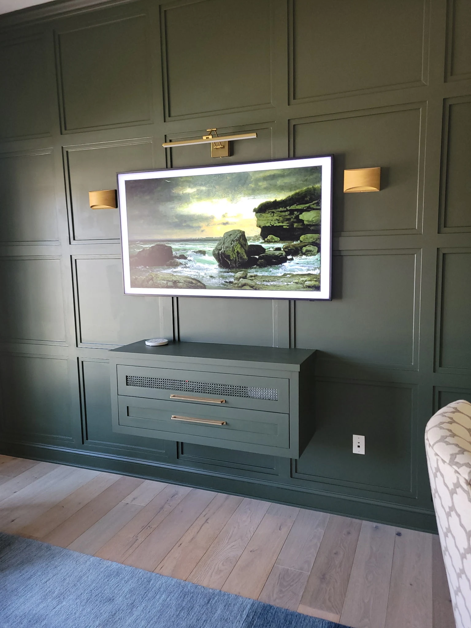 Dark green paneled accent wall with mounted television, brass lighting, and custom wall-mounted cabinet for den remodel in Carmel Indiana.