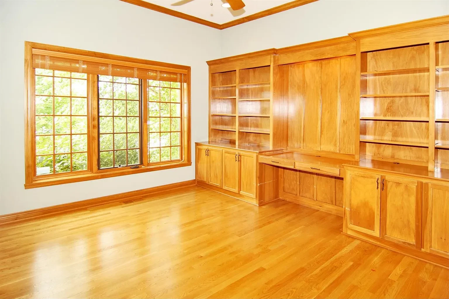 Original home office with traditional wood built-in bookcases, desk cabinetry, and wood flooring before the remodel.