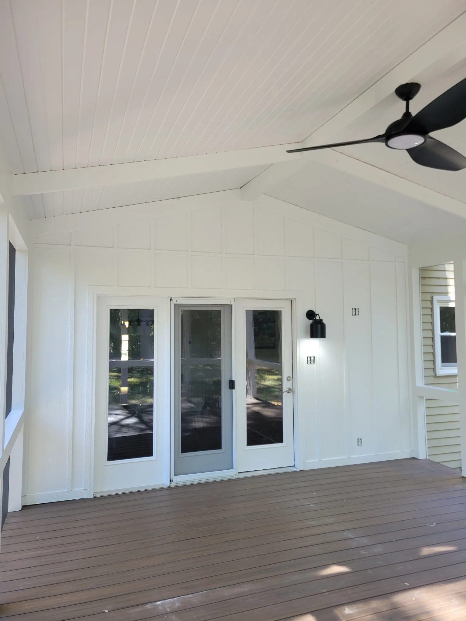 Finished screened porch interior with Trex flooring, white ceiling, ceiling fan, and entry doors