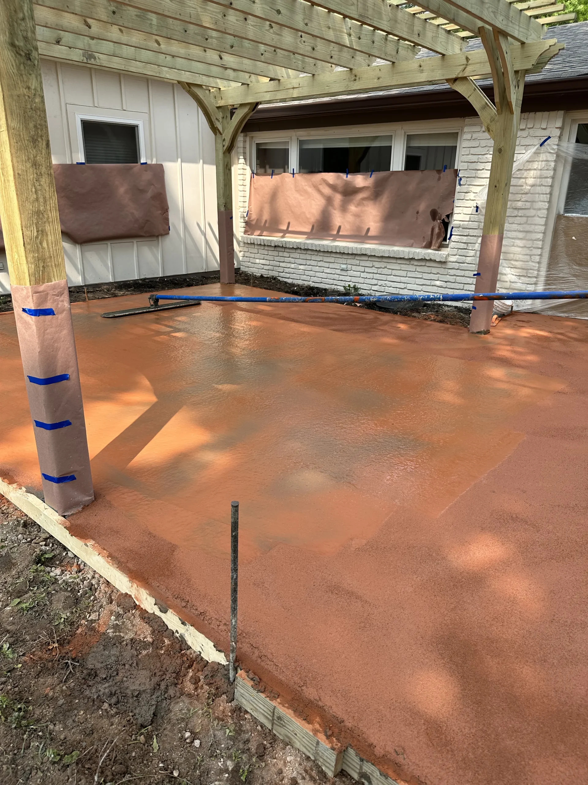 Fresh Terracotta-colored concrete being finished beneath a custom wood pergola in Carmel, Indiana