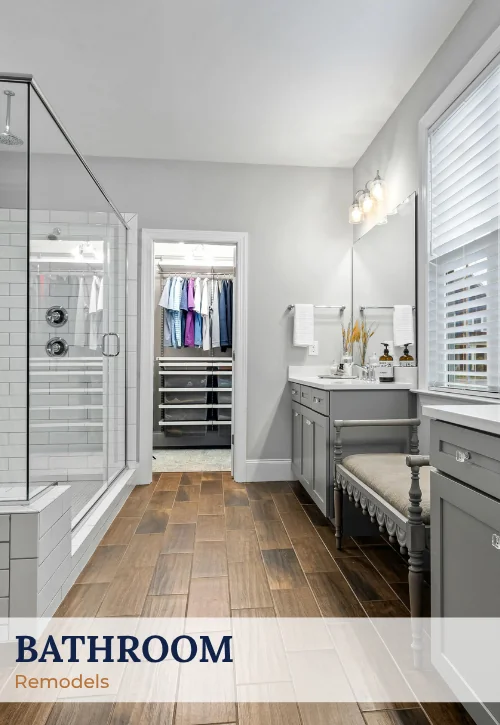 Remodeled primary bathroom with glass shower, gray vanity, wood-look tile floor, and bright natural light