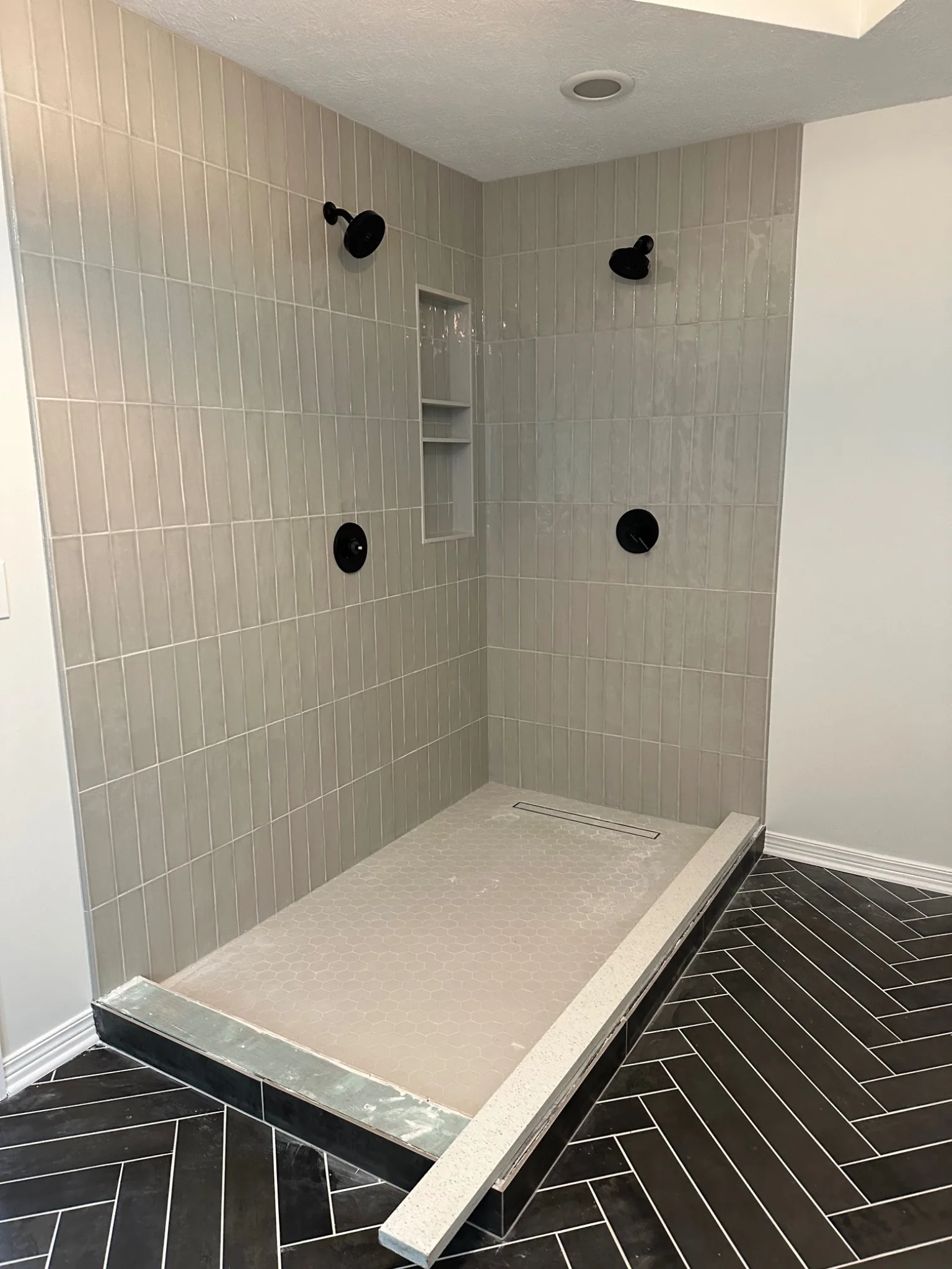 Remodeled primary bathroom shower with vertical tile, dual showerheads, niche, and linear drain in Carmel Indiana