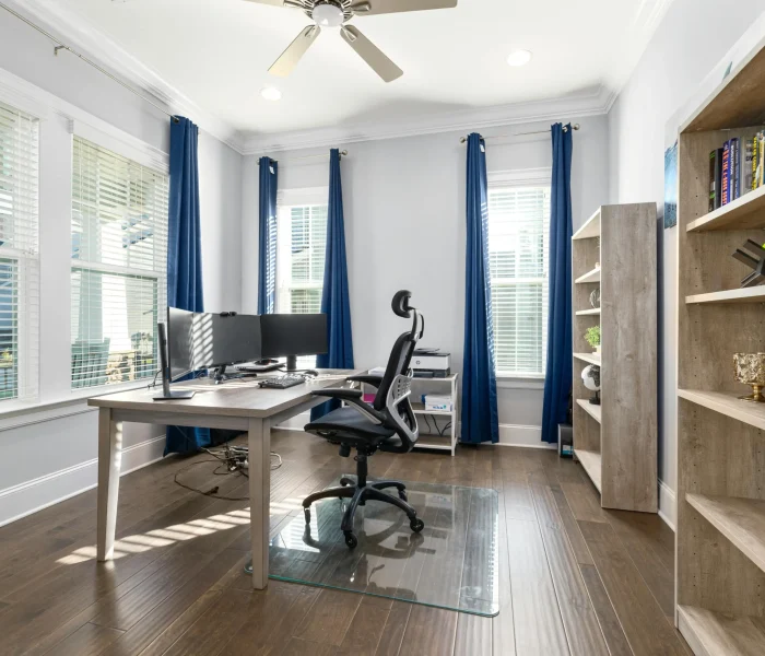 right home office with multiple windows, blue curtains, natural light, wood shelving, and desk near window