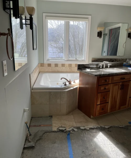 Primary bathroom before remodeling with a corner tub, wood vanity, and beige tile finishes